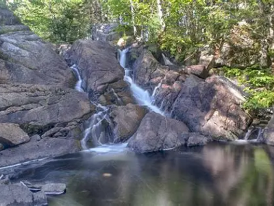 Image of Pockwock Falls with multiple small flows over rocks with trees in the background and a small water pool in the foreground